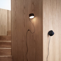 "Modern wall lamp in rich brown and sleek black against a warm wood backdrop, showcasing minimalist design."