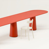 Red elongated table with rounded edges and solid red legs, paired with a simple white chair.