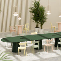 Green oval table with black base surrounded by pastel chairs in pink, yellow, and green. Modern interior design.