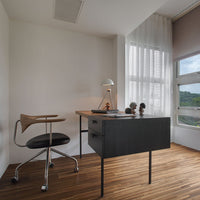 Modern office setup with a sleek black desk, wooden flooring, and a chrome chair, enhanced by soft natural light.