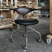 "Black upholstered swivel chair with sleek wood backrest and silver metal base, featuring a modern design."
