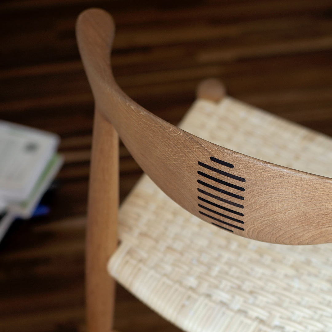 Natural wood chair with a matte finish and a woven seat, featuring a black striped pattern on the curved backrest.