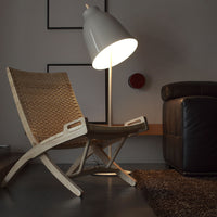 "Woven rattan chair in natural tones, paired with a sleek white lamp and dark leather sofa, on a textured rug."
