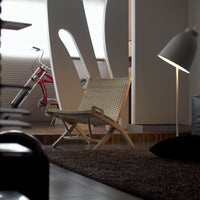 Light beige rattan chair on a dark brown rug, complemented by a soft gray lamp and white interior details.