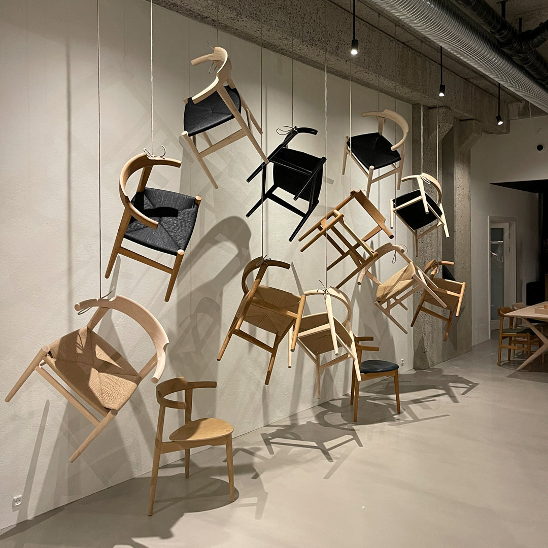 "Assorted wooden chairs in light brown with black and natural fabric accents, hanging artfully on a wall."