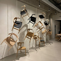 "Assorted wooden chairs in light brown with black and natural fabric accents, hanging artfully on a wall."