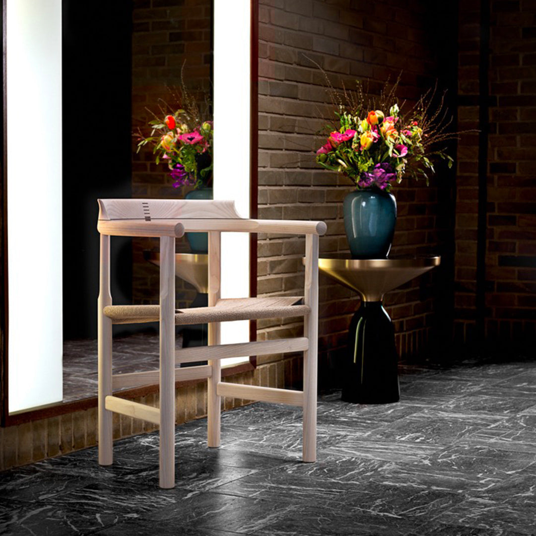 Light wood bar stool with a minimalist design against dark marble flooring and vibrant floral arrangement.