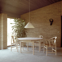 Light wood dining table and chairs with a simple, neutral design; warm brick wall and soft natural lighting.