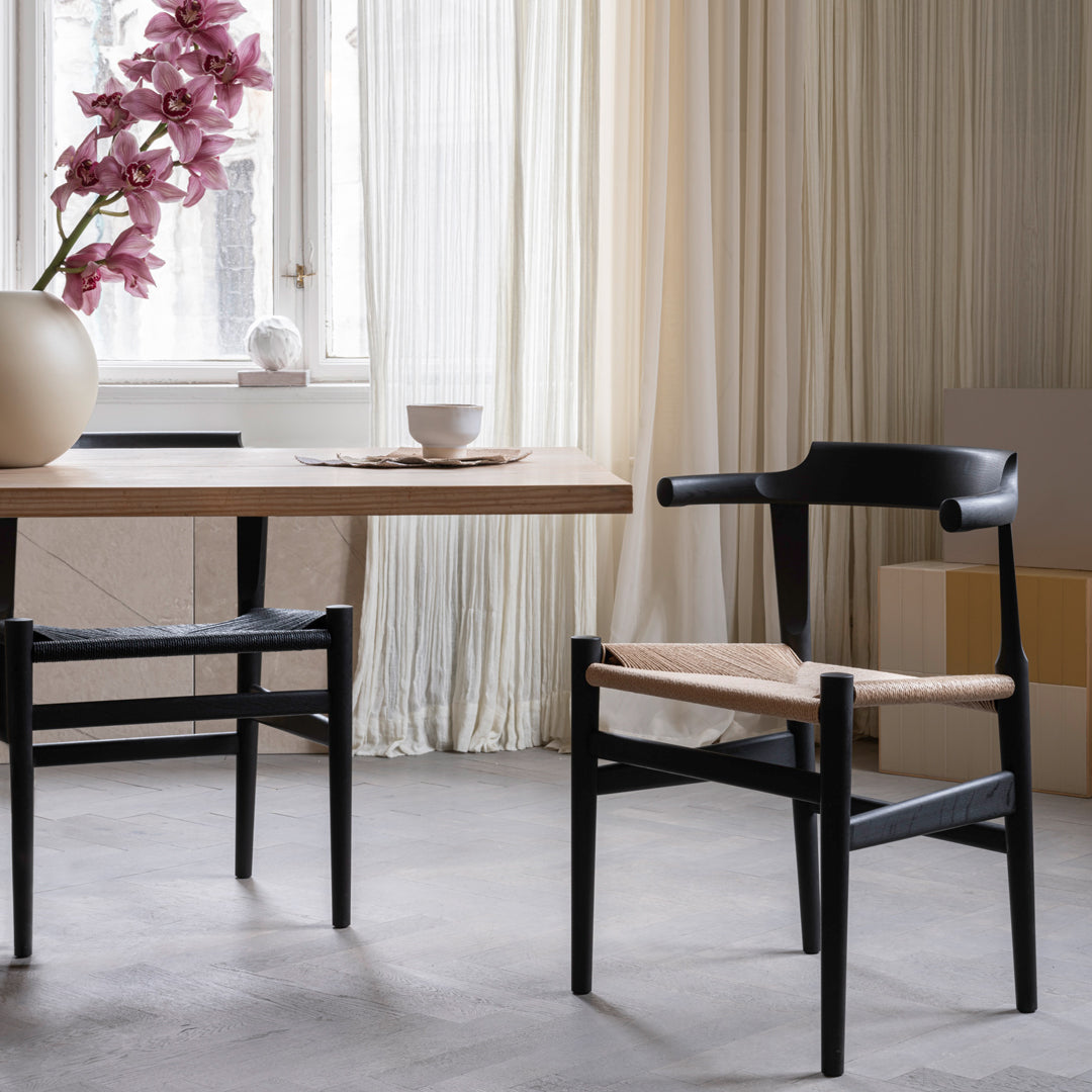Black wooden chair with natural beige seat, stylishly complementing a light wood table and soft, neutral-toned decor.