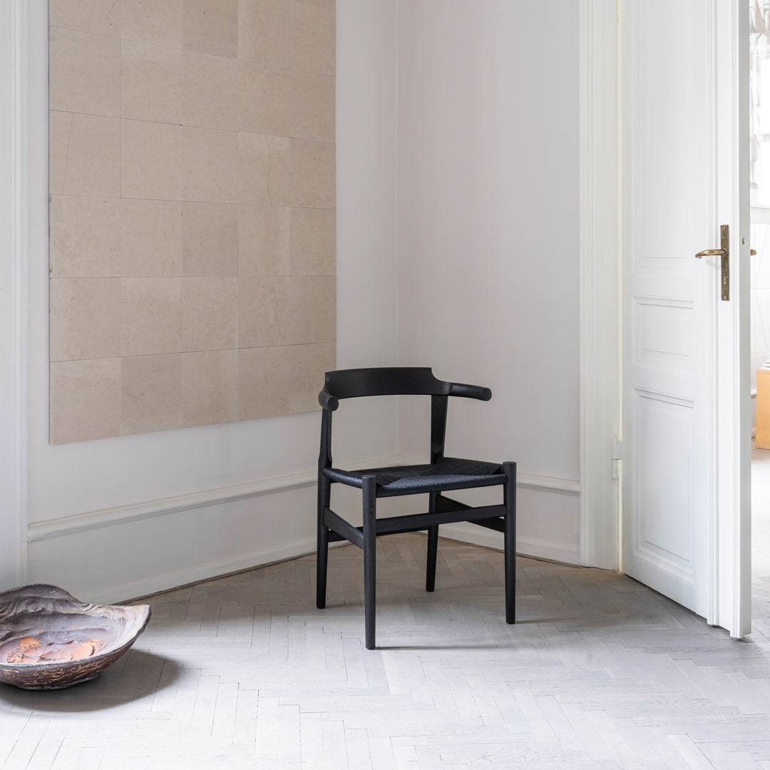 "Modern black chair with sleek lines against a neutral wall, highlighting minimalist design and elegance."