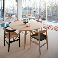 Light wood round table with black and natural finish chairs, set against a backdrop of neutral tones and colorful striped rug.