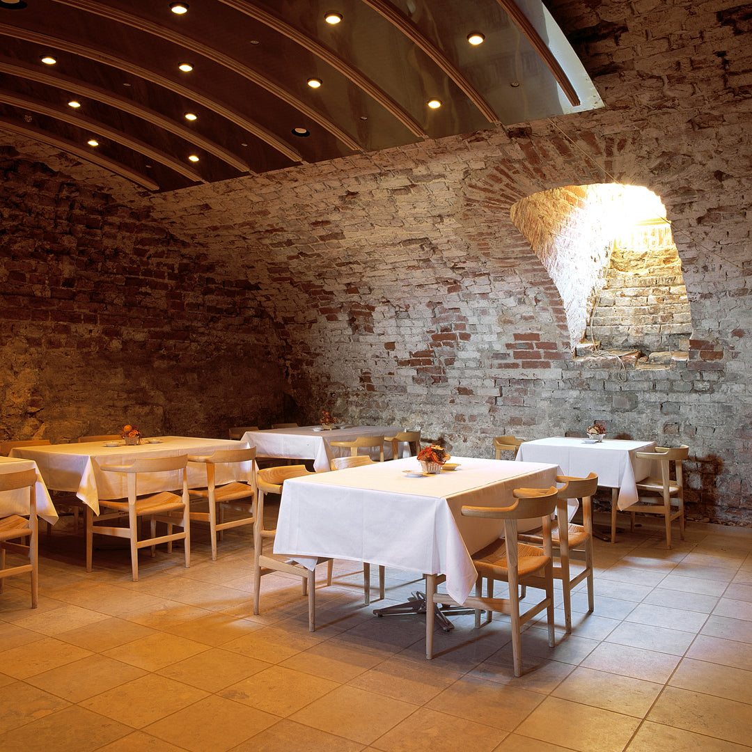 "Warm earthy tones with rustic brick walls, wooden tables, and bright white tablecloths create a cozy dining atmosphere."