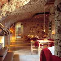 Cozy restaurant interior featuring warm stone walls, wooden accents, and red tablecloths paired with neutral tones.