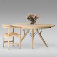 Light wood round table with a minimalist design, featuring natural tones and a unique geometric base paired with a simple chair.