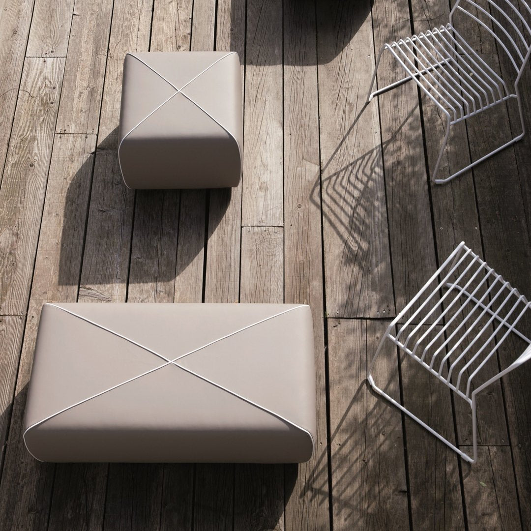 Beige outdoor poufs with decorative cross patterns, set on a wooden deck beside white wire chairs.
