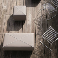 Beige outdoor poufs with decorative cross patterns, set on a wooden deck beside white wire chairs.