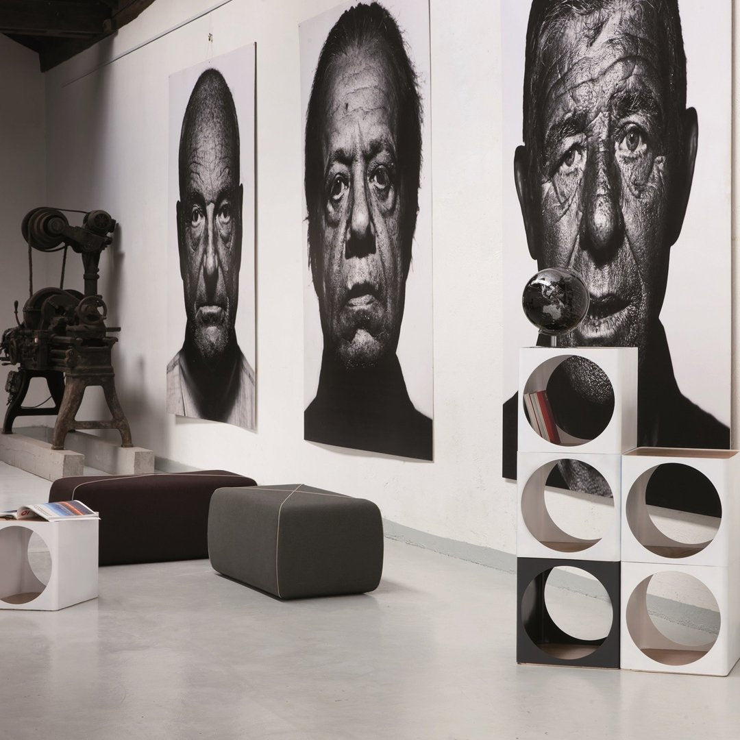 Modern interior with black and white wall art, gray ottoman, and white cubes featuring circular cutouts.