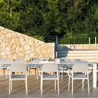 Modern outdoor dining set featuring sleek white chairs and a table against a natural stone backdrop and green foliage.