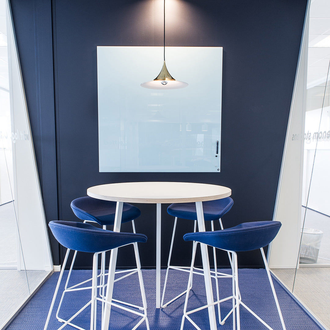 Modern round table with white legs and a light wood top, surrounded by navy blue upholstered chairs in a sleek white space.