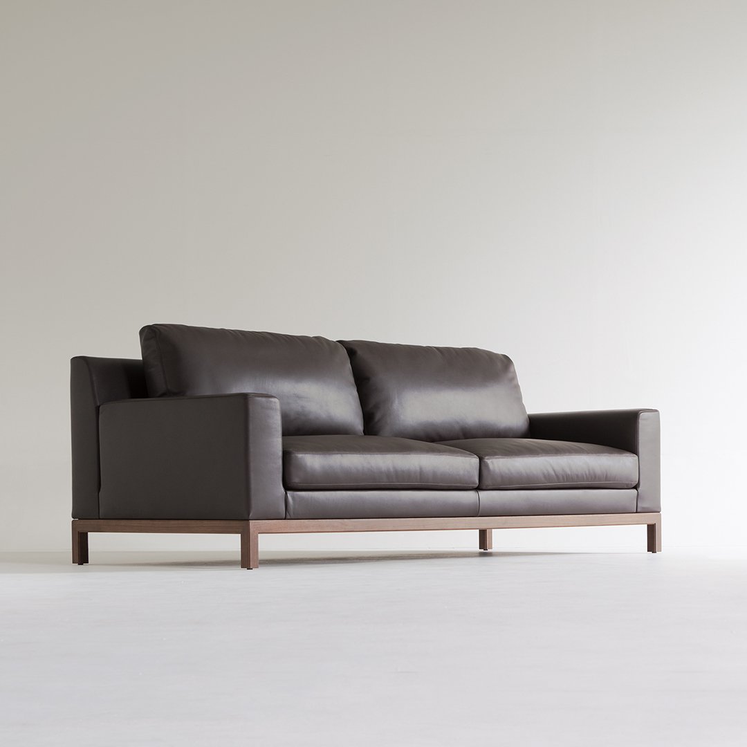 Dark brown leather sofa with minimalist design and wooden base, enhancing modern interior aesthetics.