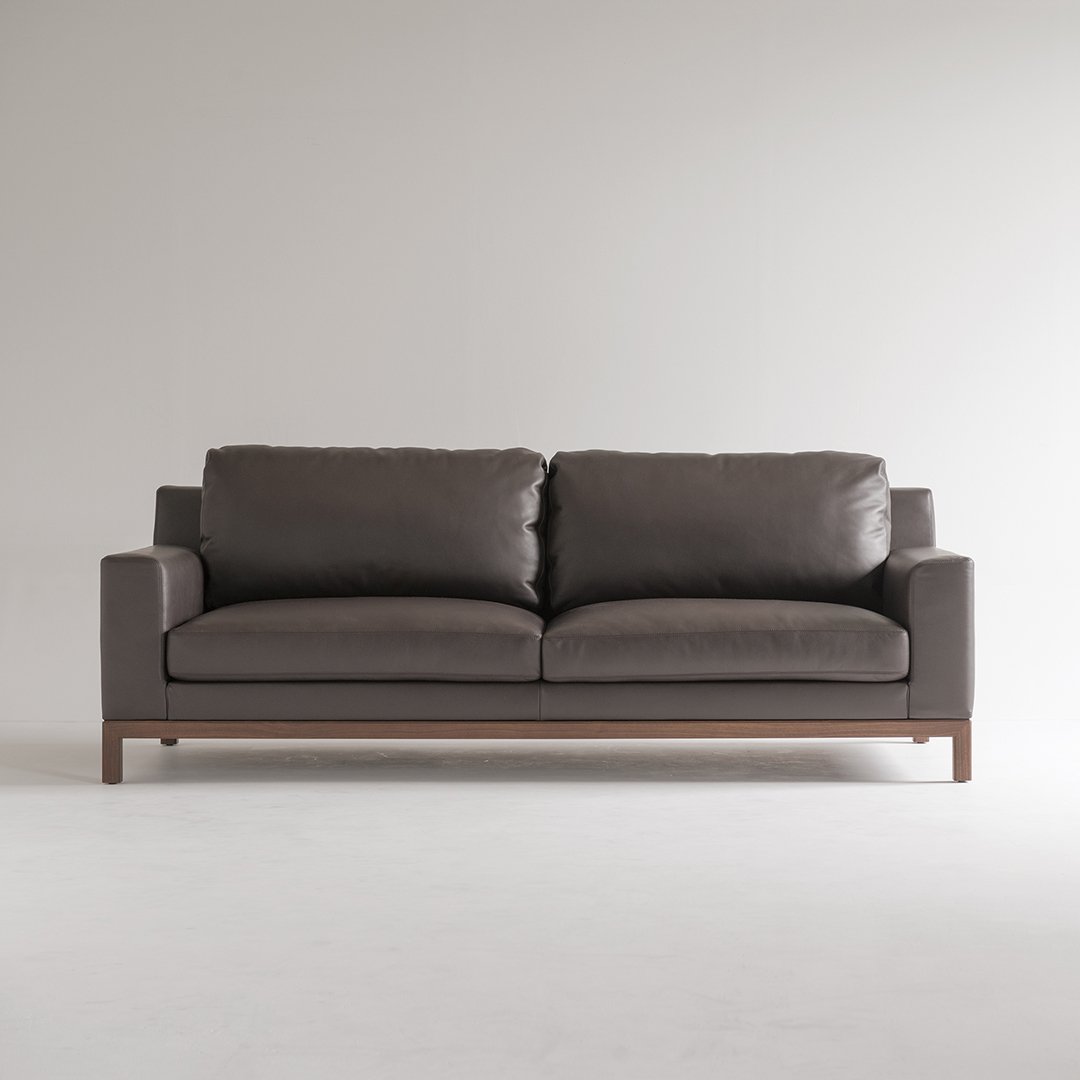 Gray leather sofa with a minimalist design and wooden legs, featuring smooth cushions and clean lines.