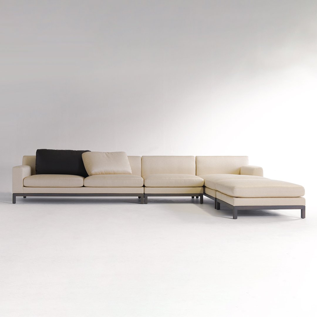 Beige sectional sofa with black accent pillow, featuring a sleek, modern design and minimalist style.