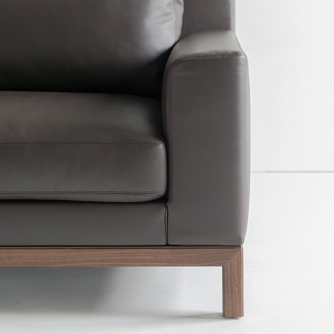 Dark gray leather sofa with a sleek, modern design and a warm wood base. Perfect for contemporary interiors.