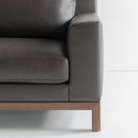 Dark gray leather sofa with a sleek, modern design and a warm wood base. Perfect for contemporary interiors.