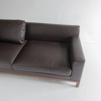 Brown leather sofa with smooth upholstery and minimalist design, featuring a dark wood frame for a modern look.