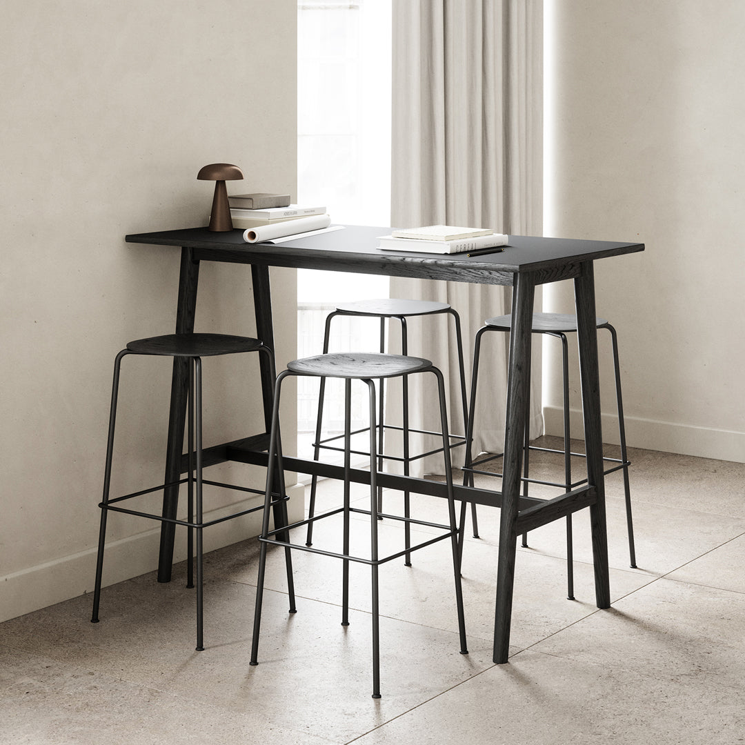Sleek black bar table with minimalist wire stools against a light beige backdrop and neutral tones.