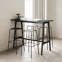 Sleek black bar table with minimalist wire stools against a light beige backdrop and neutral tones.