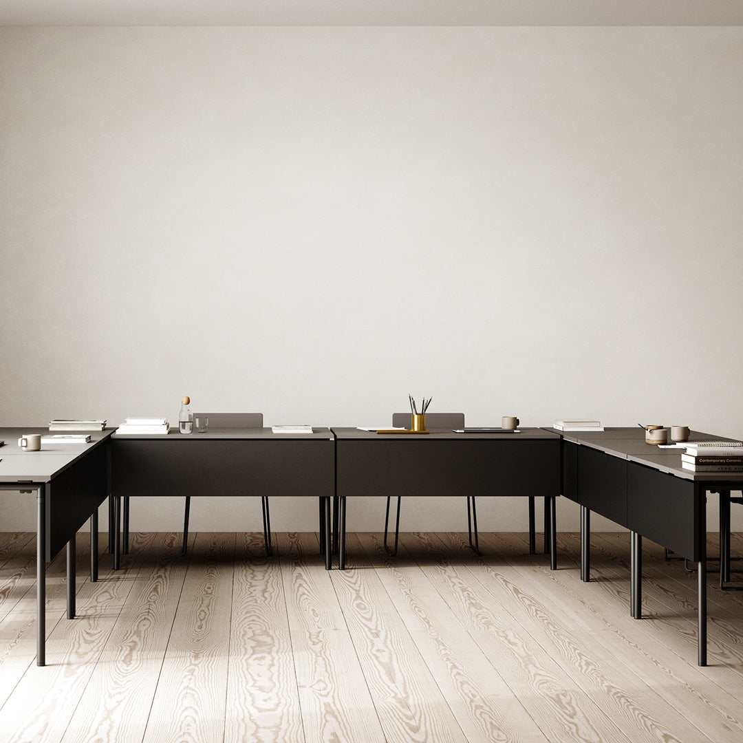 "Minimalist black desk set on light wood flooring with a neutral wall backdrop, emphasizing clean lines and simple patterns."