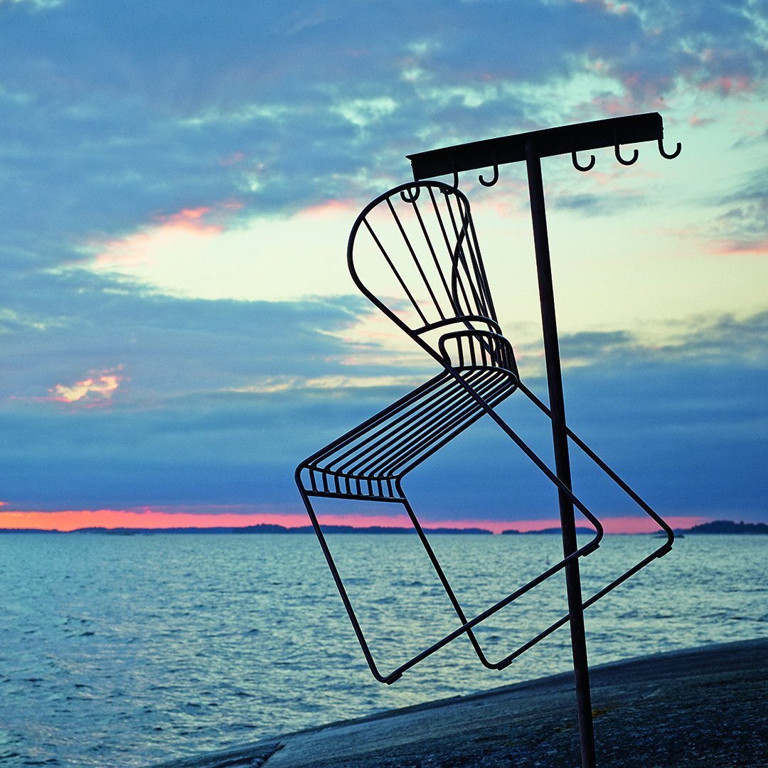Black wire chair silhouette against a vibrant twilight sky with pink and blue hues, showcasing a scenic waterfront backdrop.