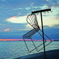 Black wire chair silhouette against a vibrant twilight sky with pink and blue hues, showcasing a scenic waterfront backdrop.