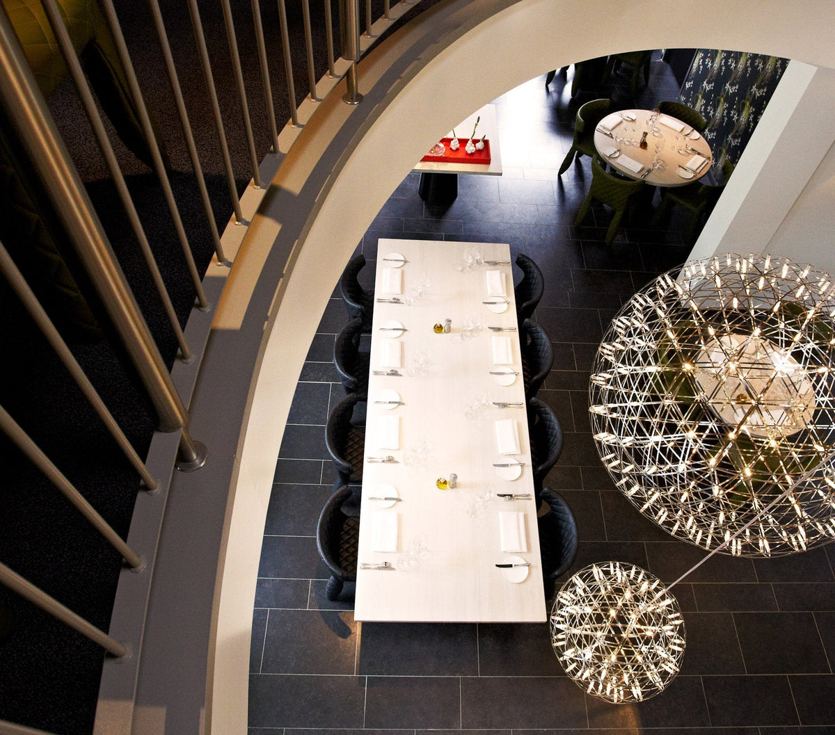 Modern dining room featuring a sleek white table, black seating, and striking decorative light fixtures against a dark floor.