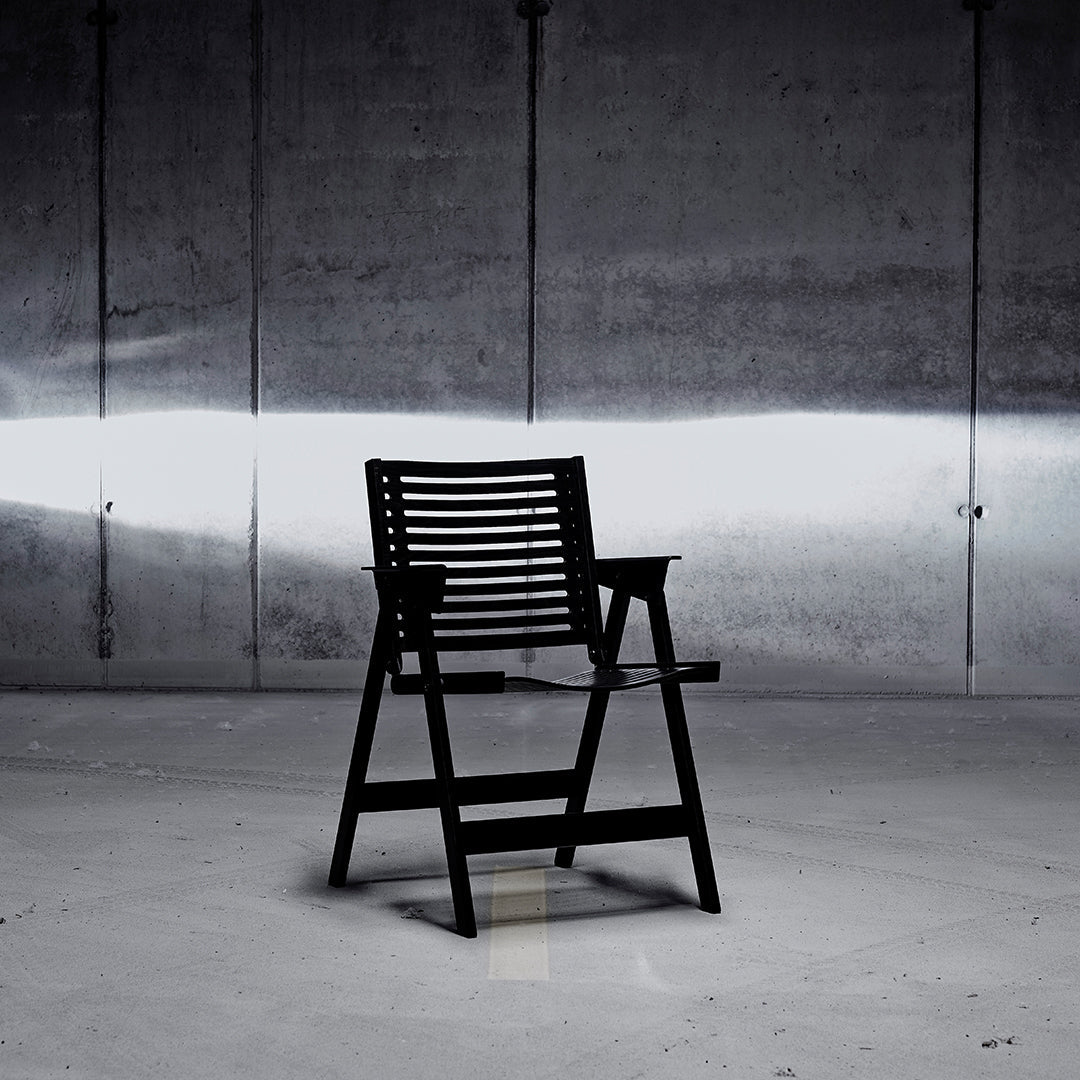 Black slatted chair against a concrete background, featuring clean lines and a modern design.
