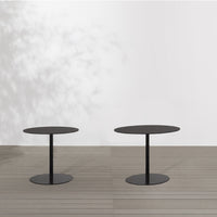 Black round coffee tables with sleek bases, set against a light backdrop and wooden flooring.