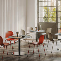 Modern dining area featuring red, beige, and gray chairs around circular tables with a natural wood floor and light walls.