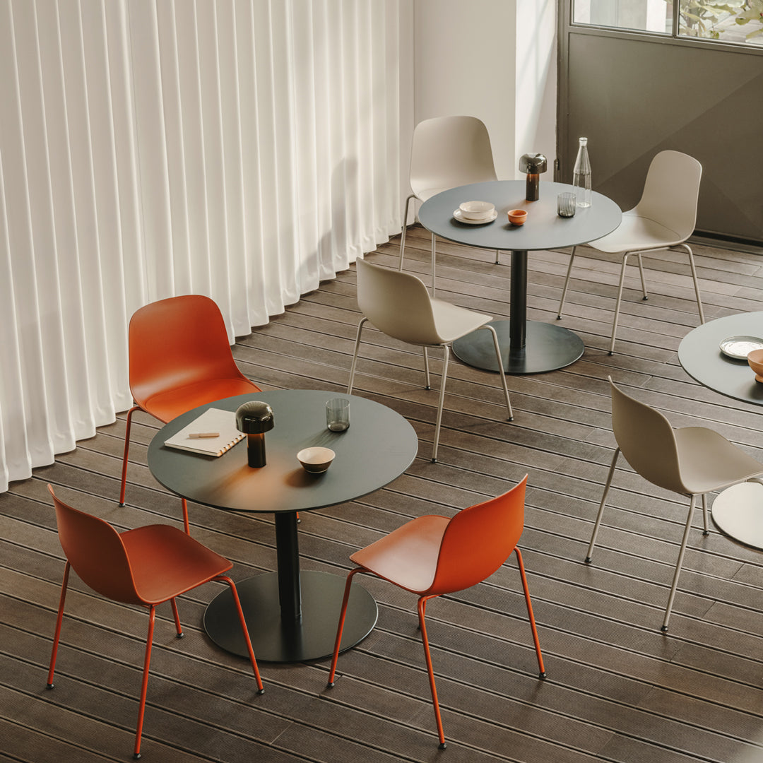 Modern dining setup featuring round black tables with orange and beige chairs against light wood flooring.