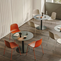 Modern dining setup featuring round black tables with orange and beige chairs against light wood flooring.