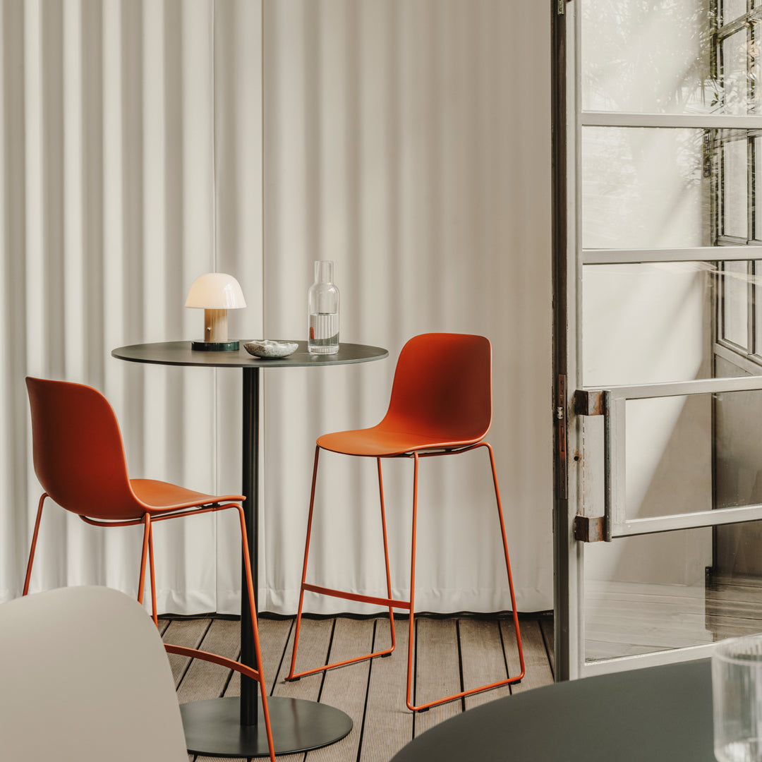 "Modern orange bar stools and sleek black table against soft white backdrop, creating a stylish and contemporary setting."