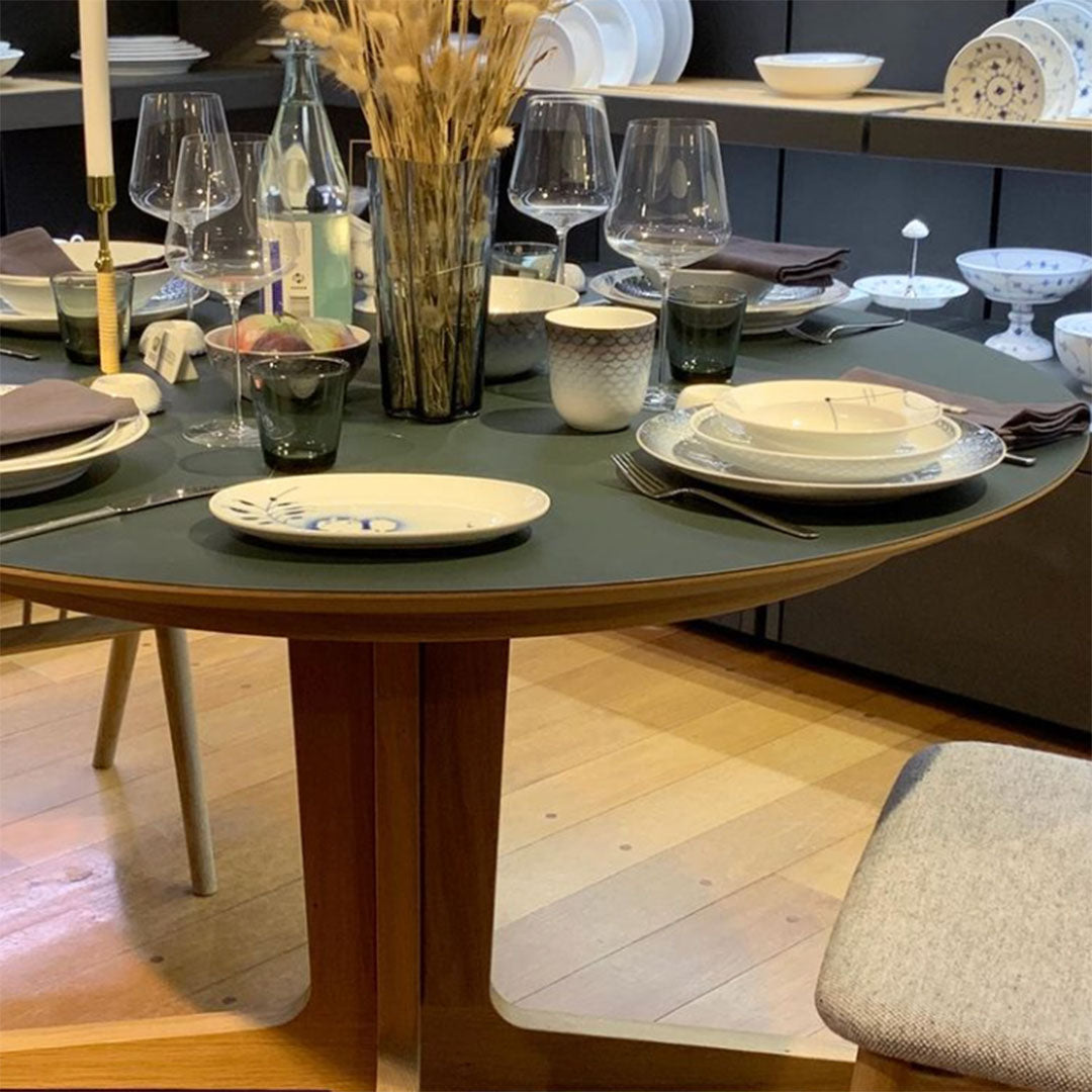 Elegant table setting featuring green tablecloth, white and blue patterned plates, glassware, and natural decor.