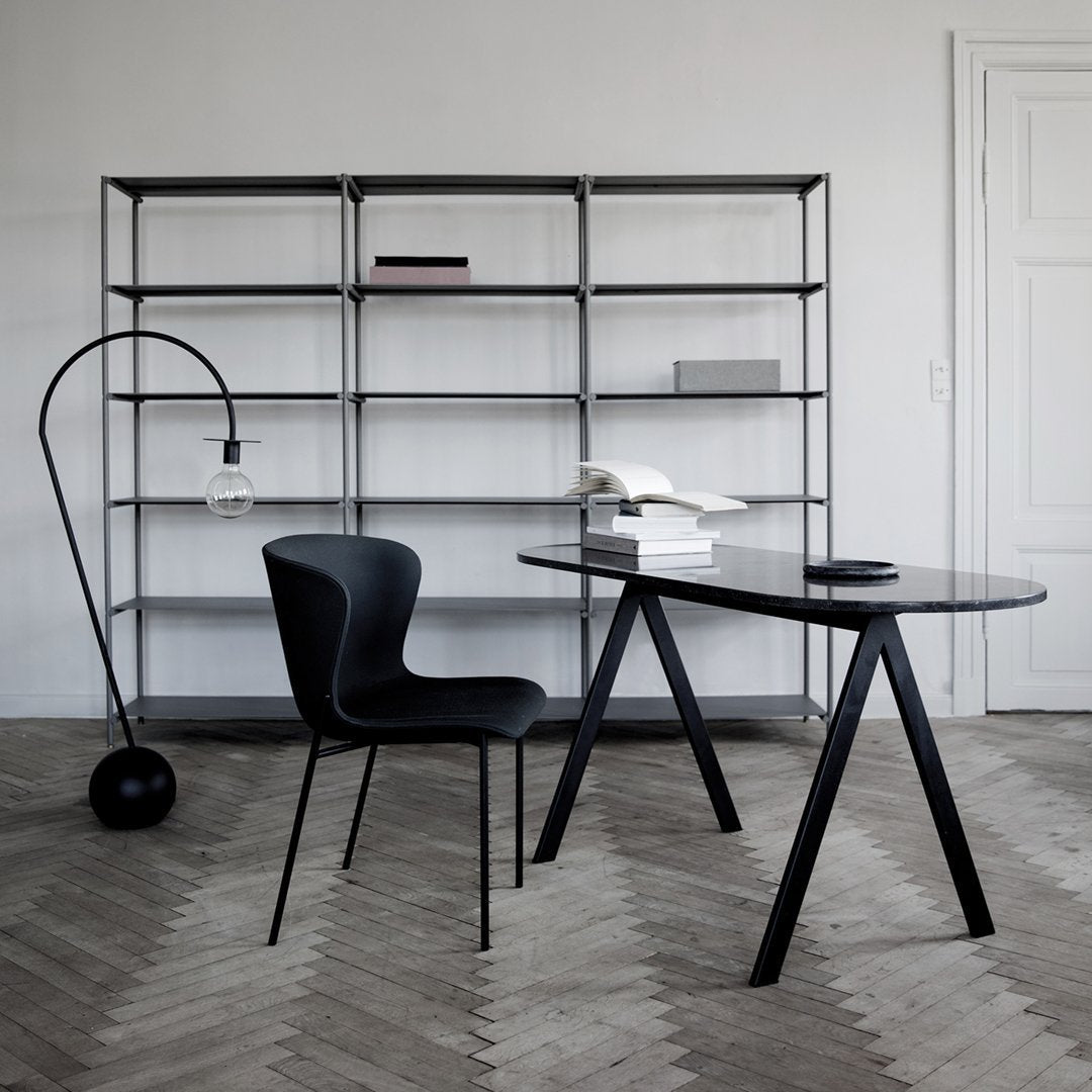 "Elegant black desk and chair set against a light grey wall with a wooden herringbone floor pattern."
