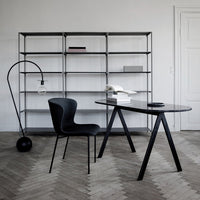 "Elegant black desk and chair set against a light grey wall with a wooden herringbone floor pattern."