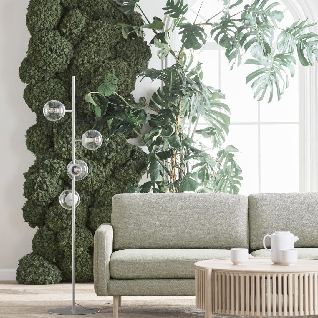 Sleek green velvet sofa paired with a natural wood coffee table and surrounded by lush greenery and modern light fixtures.
