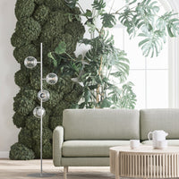 Sleek green velvet sofa paired with a natural wood coffee table and surrounded by lush greenery and modern light fixtures.