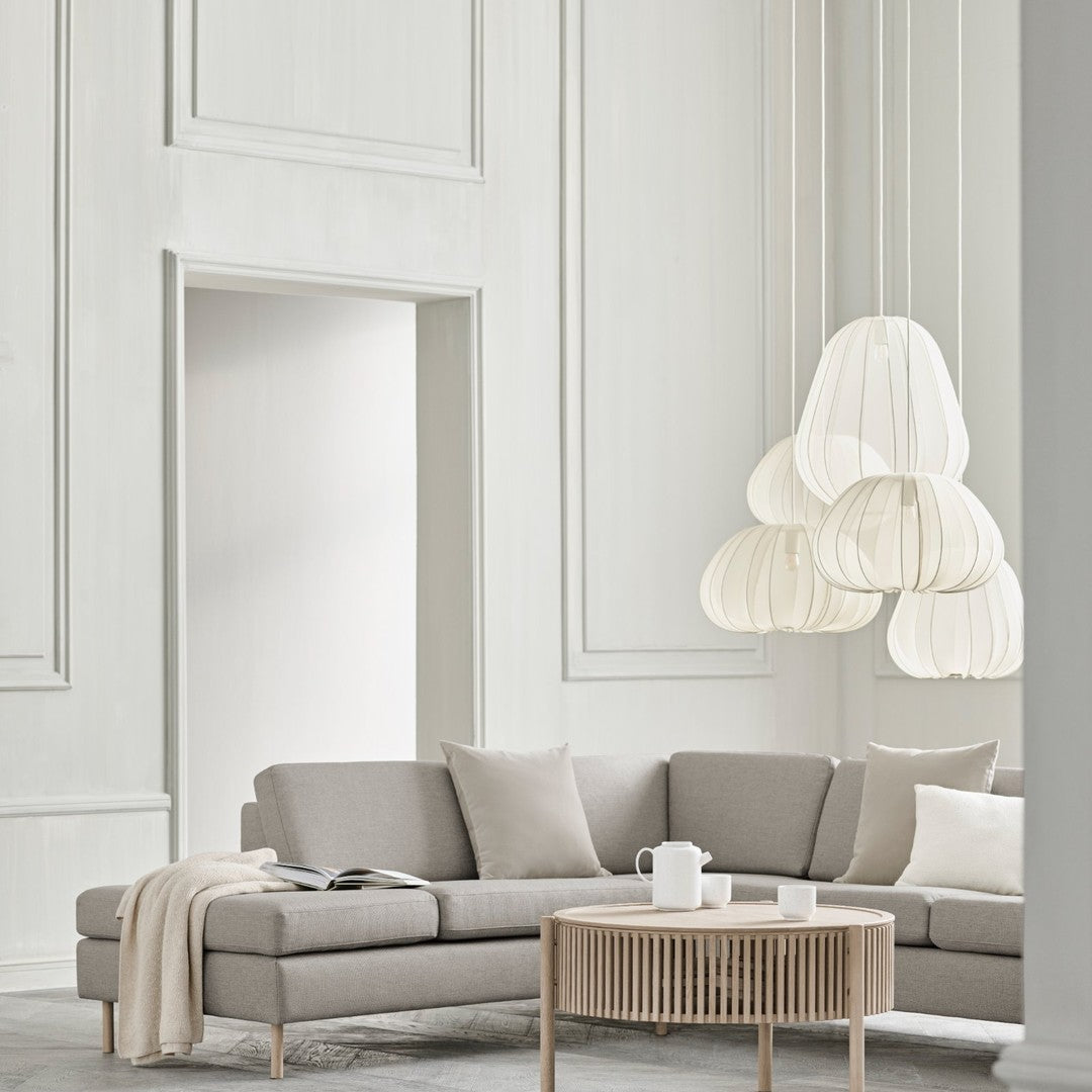 Light gray sofa with soft beige cushions, complemented by a neutral-toned, layered pendant light in a minimalistic setting.