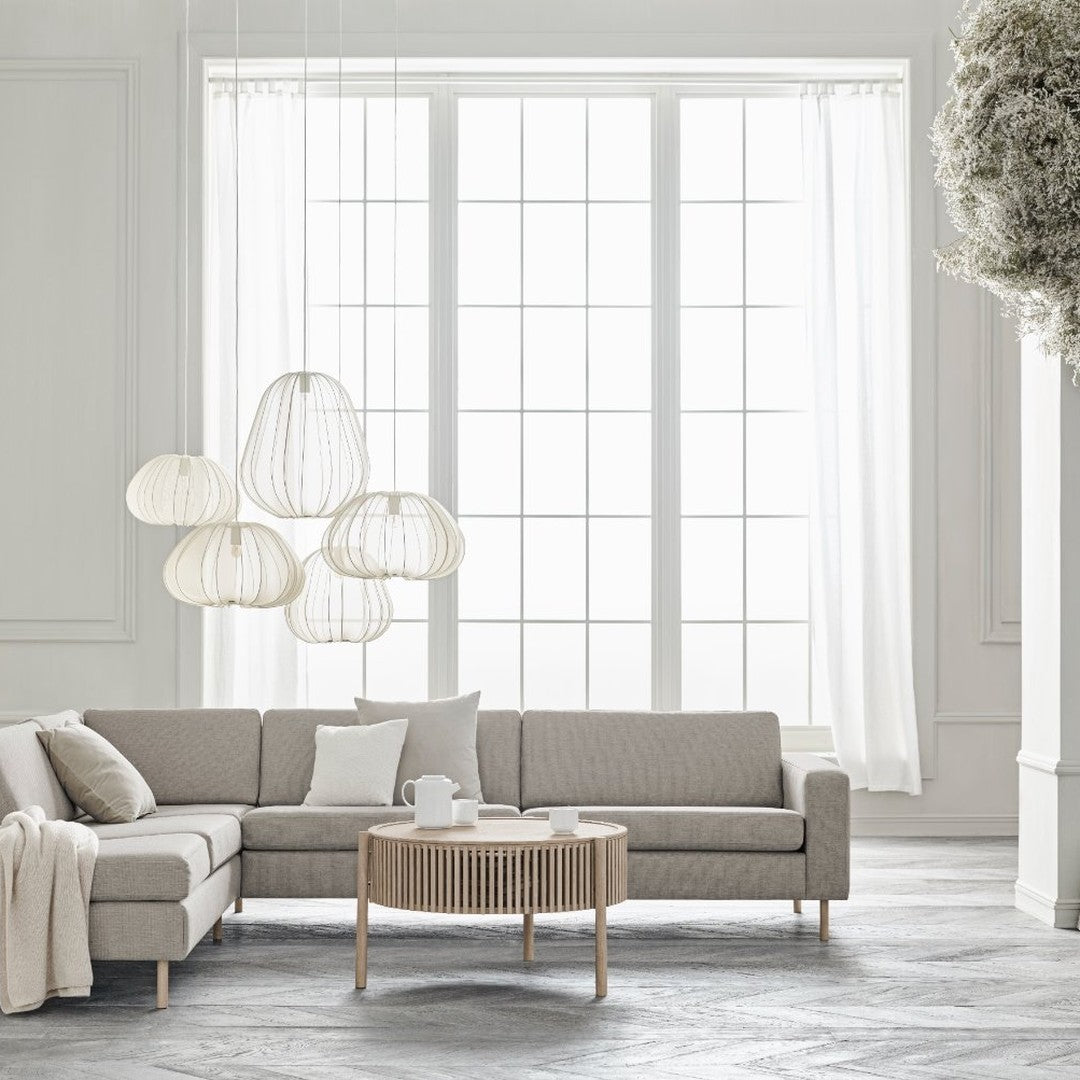 Light grey sectional sofa with neutral throw pillows, paired with a round wooden coffee table and white hanging lamps.