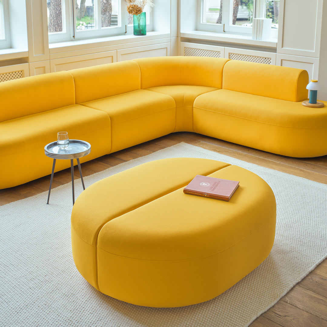 Bright yellow sectional sofa with smooth curves and a matching round coffee table on a light-colored area rug.