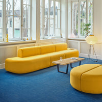 Bright yellow modern sofa with smooth curves, paired with a round coffee table on a textured blue carpet.